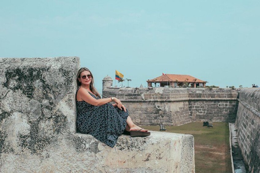 A person sitting on a stone wall overlooking a historical fortification with a flag and a building in the background. 3