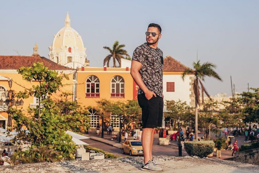 A person standing in front of a yellow building with a dome, palm trees, and a busy street. 2