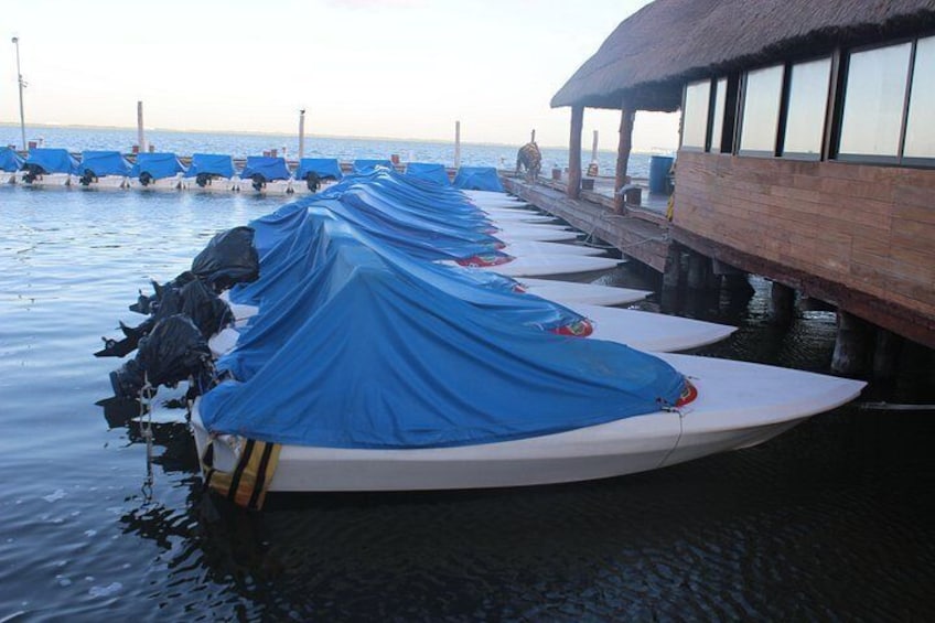 A row of covered boats docked at a pier with a thatched-roof structure. 1
