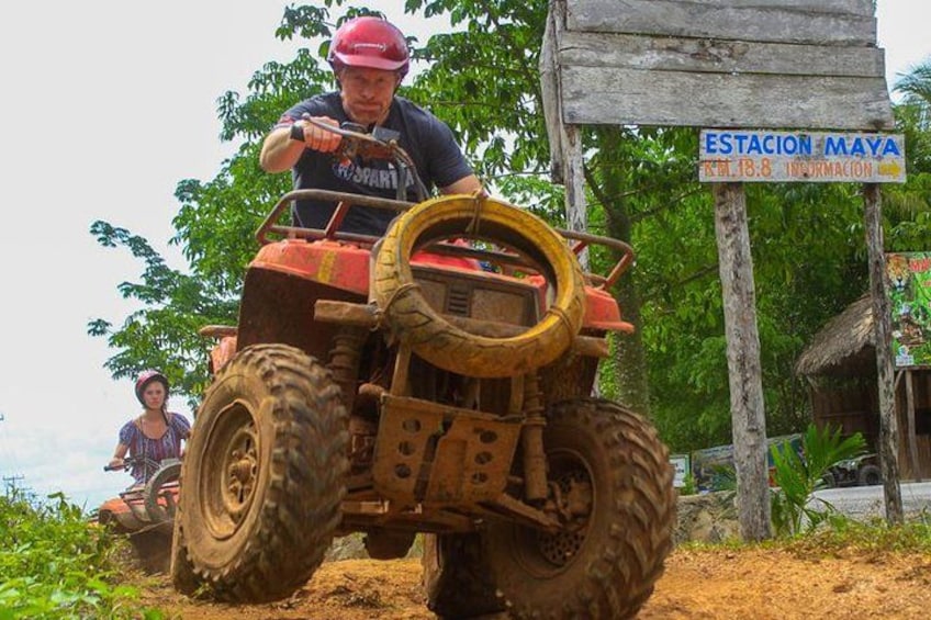 Une personne conduit un quad rouge sur un chemin de terre, et on peut voir au fond un panneau indiquant « ESTACION MAYA ». 1