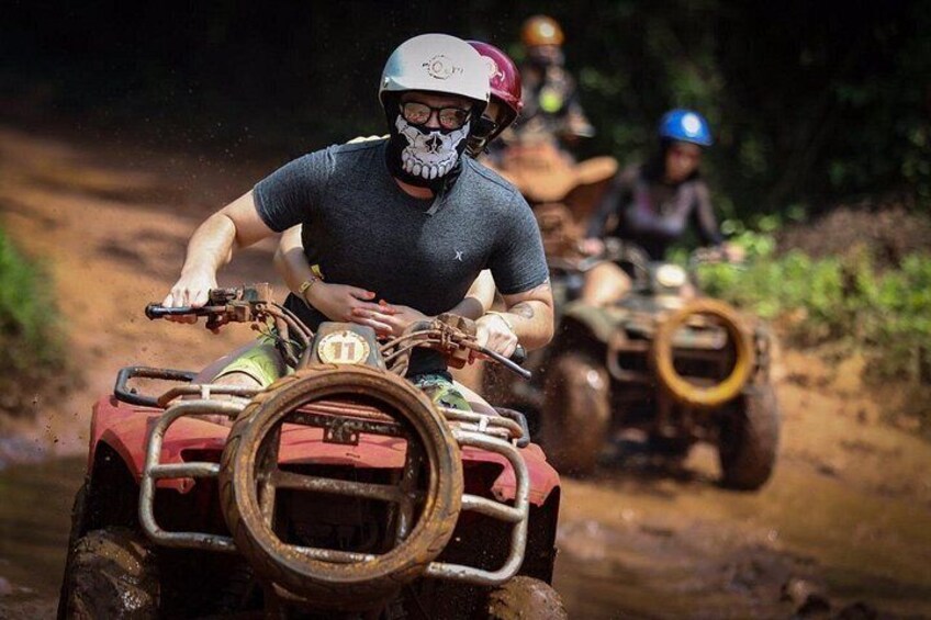 A person riding an ATV on a muddy trail with another ATV in the background. 4