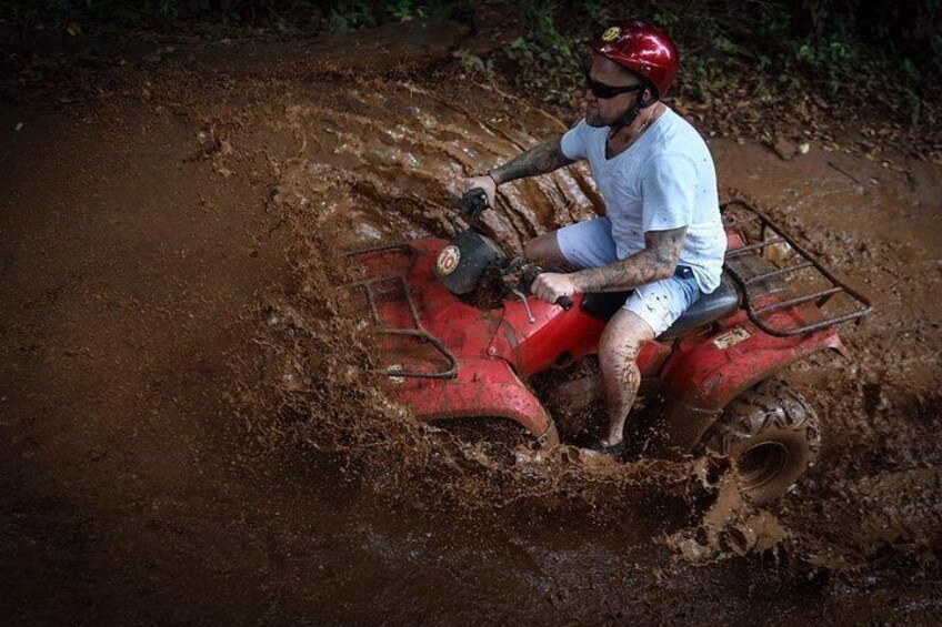 A person riding a red ATV through a muddy terrain. 5