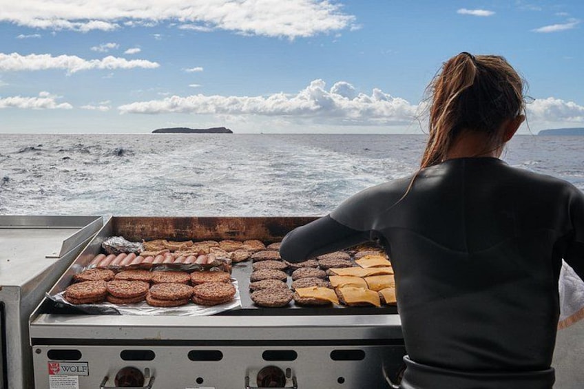 A person grilling sausages on a boat with the ocean and a distant island in the background. 5