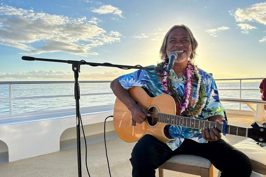 En person spelar gitarr på en båt, med ett mikrofonstativ framför sig, och havet syns i bakgrunden. 2