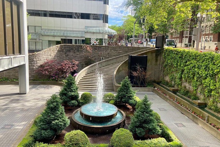 Un jardin aménagé avec une fontaine centrale, entouré d’arbustes et d’arbres aux formes soignées, et un chemin sinueux menant à l’entrée d’un bâtiment. 3