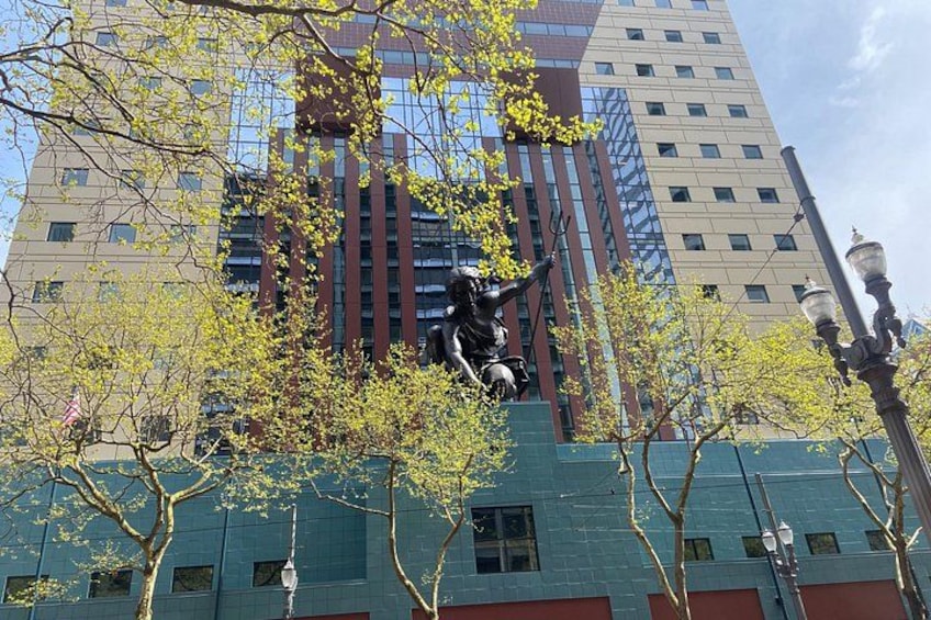 Une statue représentant une personne, située dans un paysage urbain avec de hauts immeubles et des arbres. 5
