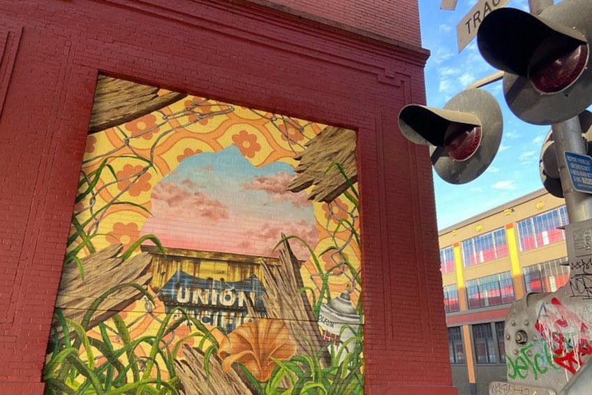 A mural with a sunset scene, a sign that reads 'Union Pacific,' and graffiti on a pole. 1