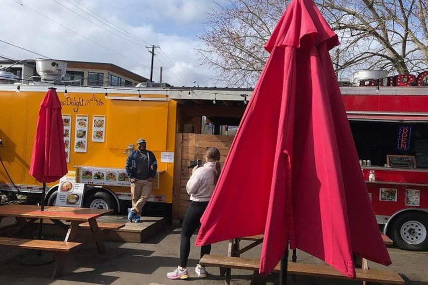 A food truck with red umbrellas, a person standing by the truck, and another person walking away. 3