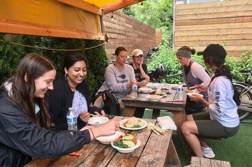 A group of people dining outdoors at a wooden table with food and drinks. 1