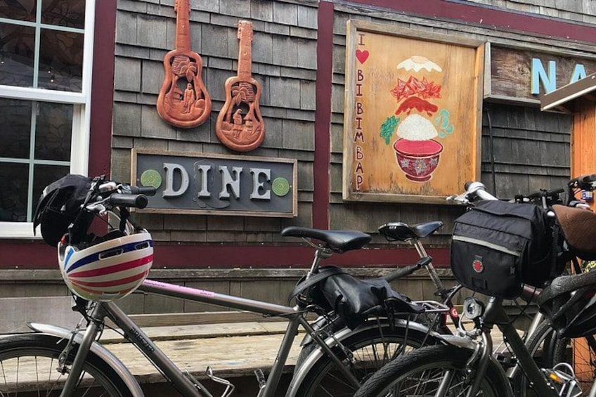 A bicycle parked in front of a restaurant with a sign that reads 'DINE' and a mural of guitars and a bowl of food. 2