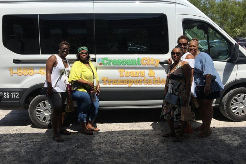 Een groep mensen poseert voor een busje, waarop 'Crescent City Tours & Transportation' staat. 3