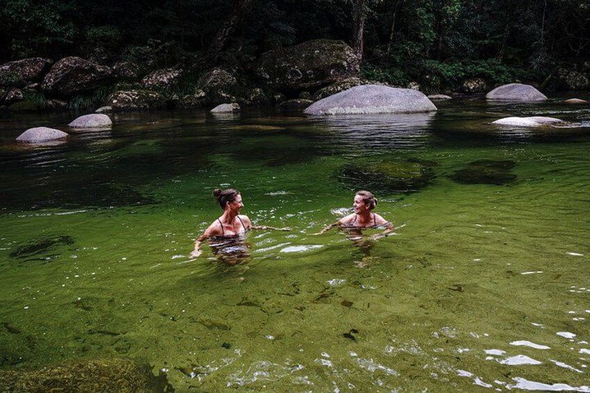 Two people swimming in a clear river surrounded by rocks and greenery. 3