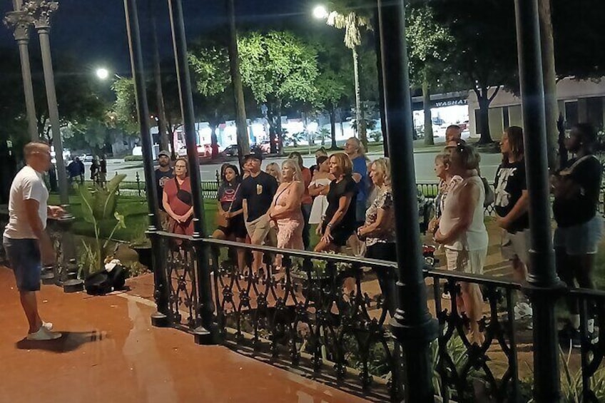 A group of people gathered around a speaker on a sidewalk at night. 4
