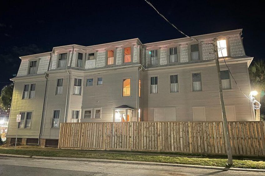 Un edificio de varios pisos con una valla de madera al frente, iluminado por farolas. 2