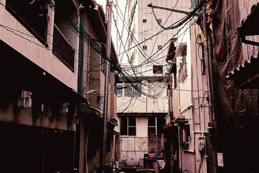 A narrow alley with buildings on either side, overcast sky, and tangled electrical wires. 2