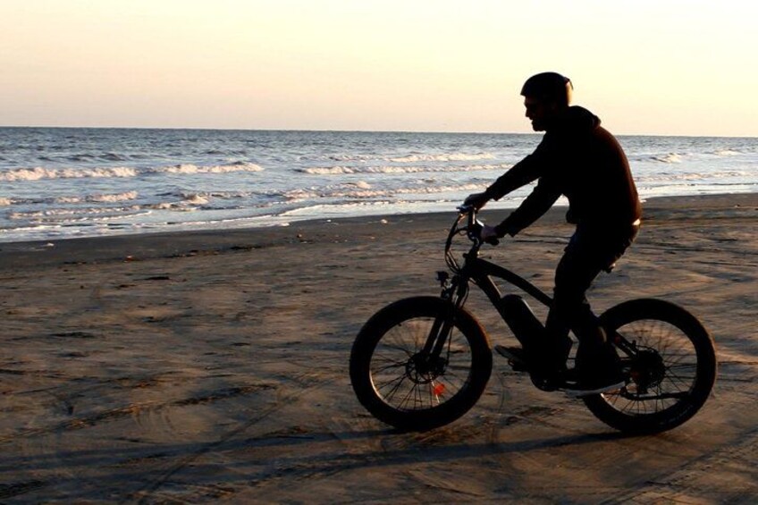 Silouette di una persona che va in bicicletta su una spiaggia al tramonto. 3