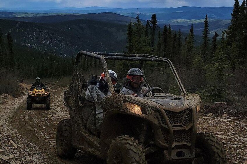 Two off-road vehicles on a dirt path surrounded by forested mountains. 4