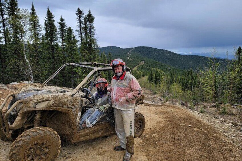A muddy off-road vehicle on a dirt path with a forested mountain background. 3