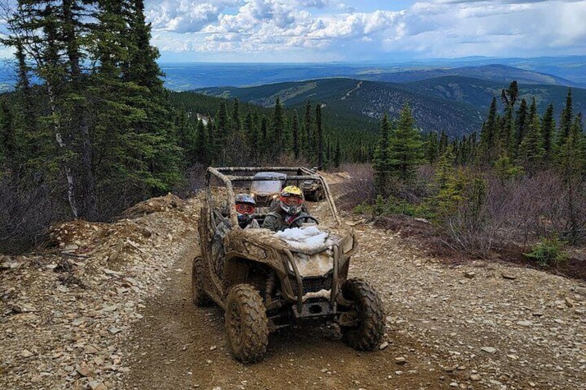 A four-wheeled off-road vehicle on a dirt path surrounded by dense forest and mountains. 5