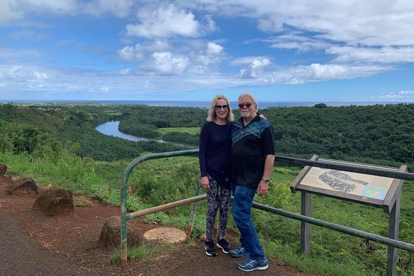 Two people standing by a railing overlooking a river and forested landscape. 5