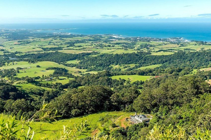 A panoramic view of a coastal landscape with rolling hills, dense forests, and a small building in the foreground. 2