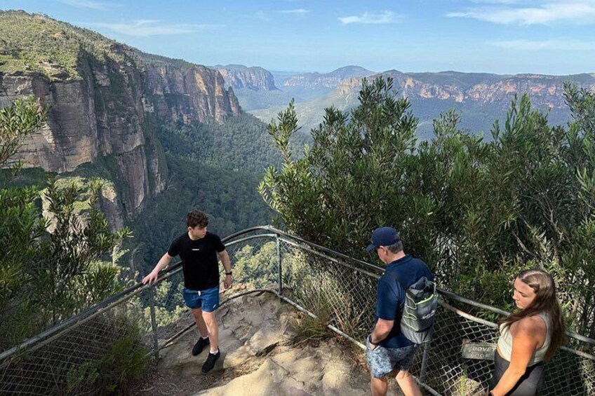 A group of people on a metal staircase overlooking a canyon with steep cliffs and dense forest. 2
