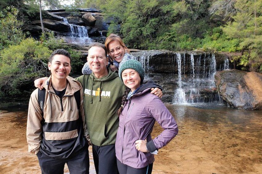 A group of people standing in front of a waterfall with lush greenery in the background. 3