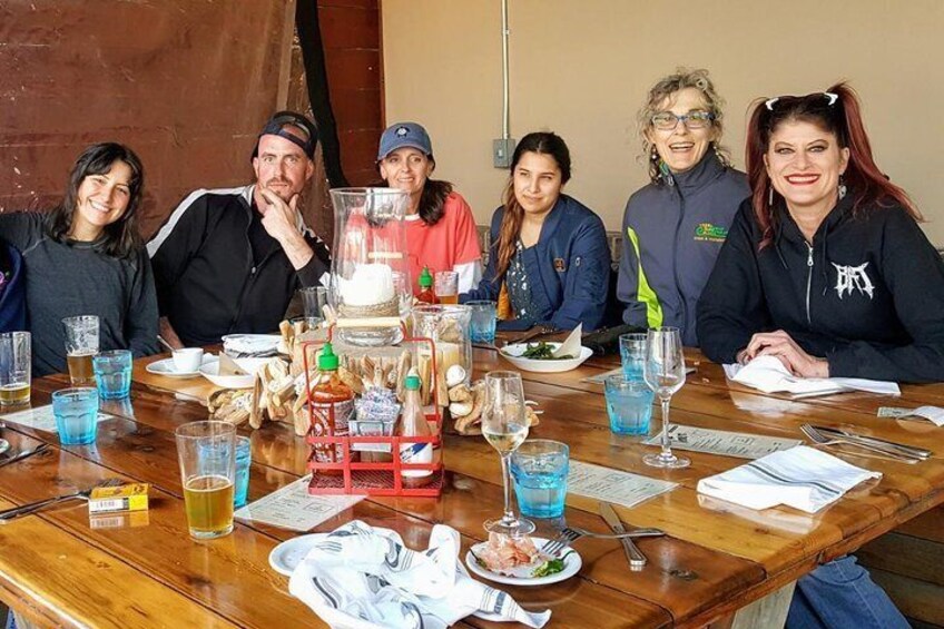 A group of people sitting around a wooden table with various drinks and food items. 2