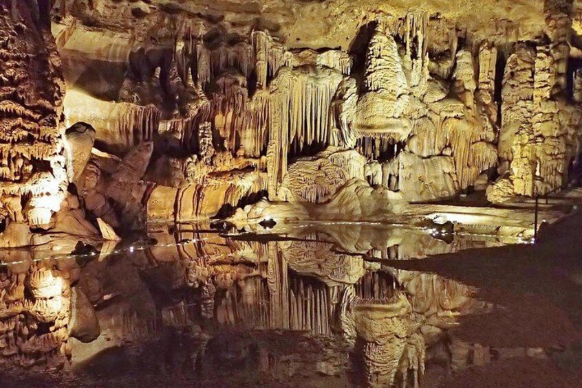 A cave with stalactites and stalagmites, a reflective water surface, and a beam of light illuminating the formations. 1