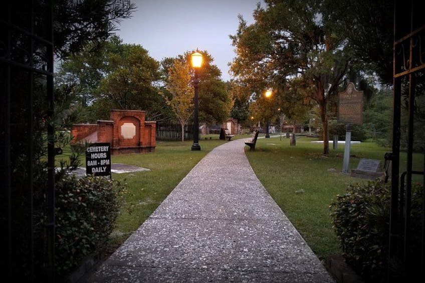 A cemetery pathway with a sign indicating hours of operation. 1