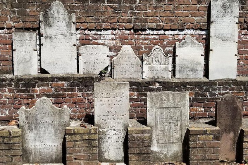 A cemetery with multiple headstones against a brick wall. 5