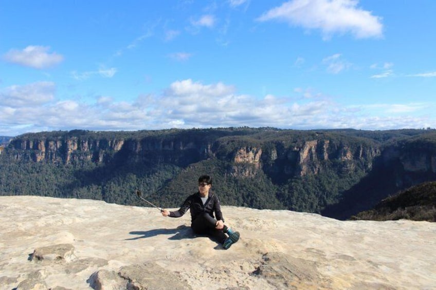 Una persona sentada sobre una roca, con una cámara, contemplando un cañón con acantilados y árboles. 1