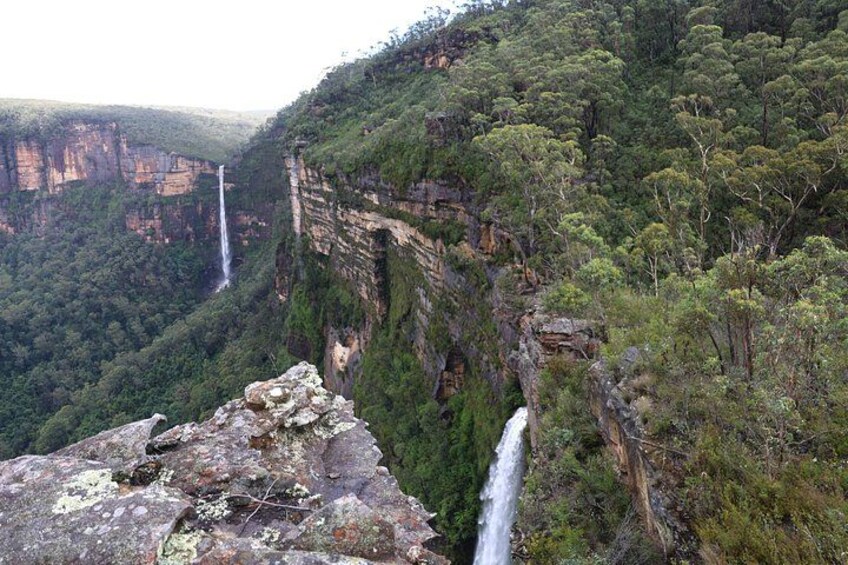A canyon with a waterfall, rocky cliffs, and dense green forest. 1