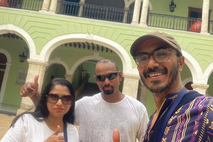 Three people posing in front of a green building with white arches. 1