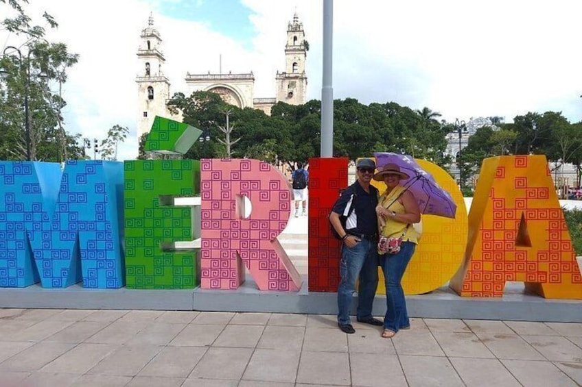Una pareja posa frente a letras coloridas que deletrean 'MEXICO', con un edificio histórico al fondo. 3