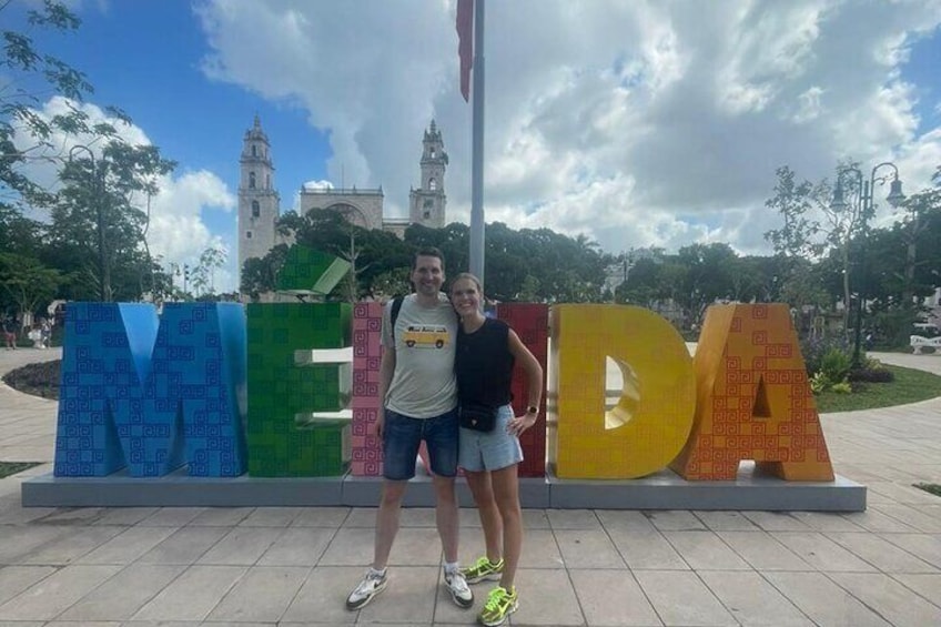 Dos personas de pie frente a un letrero colorido con las letras 'MEIDA'. 1