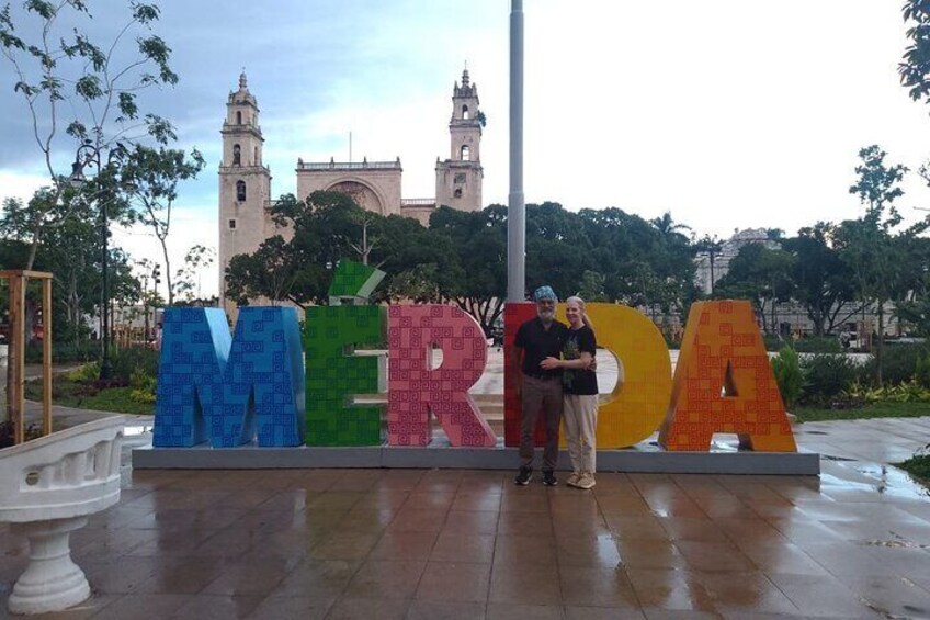 Un letrero grande al aire libre con las letras MERDA, un edificio histórico con torres y una persona parada frente al letrero. 4