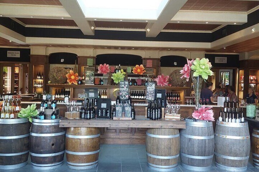 A bar with wooden barrels, a counter with bottles, and decorative flowers. 5