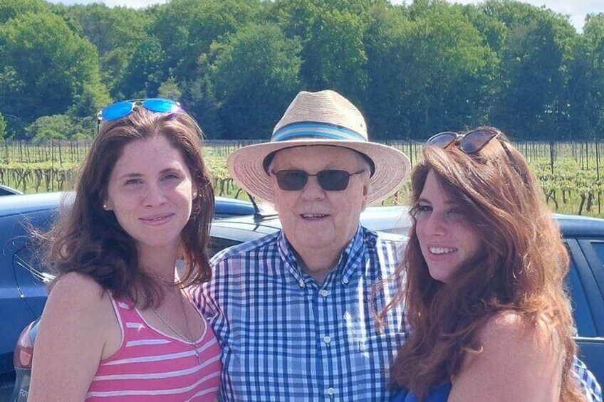 Three people posing in front of a car with a vineyard in the background. 4