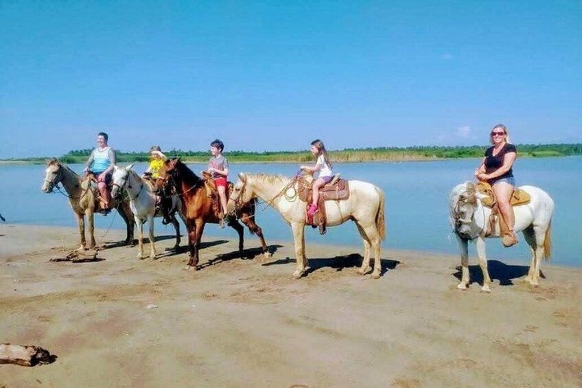 A group of people riding horses along a riverbank. 1