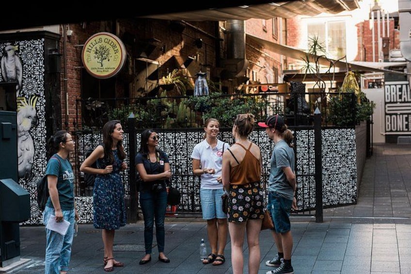 A group of people standing outside a restaurant with a decorative fence and a sign that reads 'HILLS CIDER.' 4