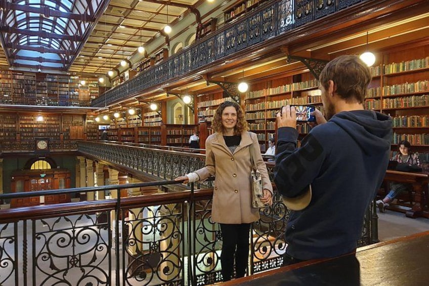 A library interior with bookshelves, a staircase, and a person taking a photo. 2