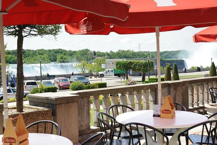 Outdoor seating with umbrellas, a waterfall in the background, and parked cars. 2