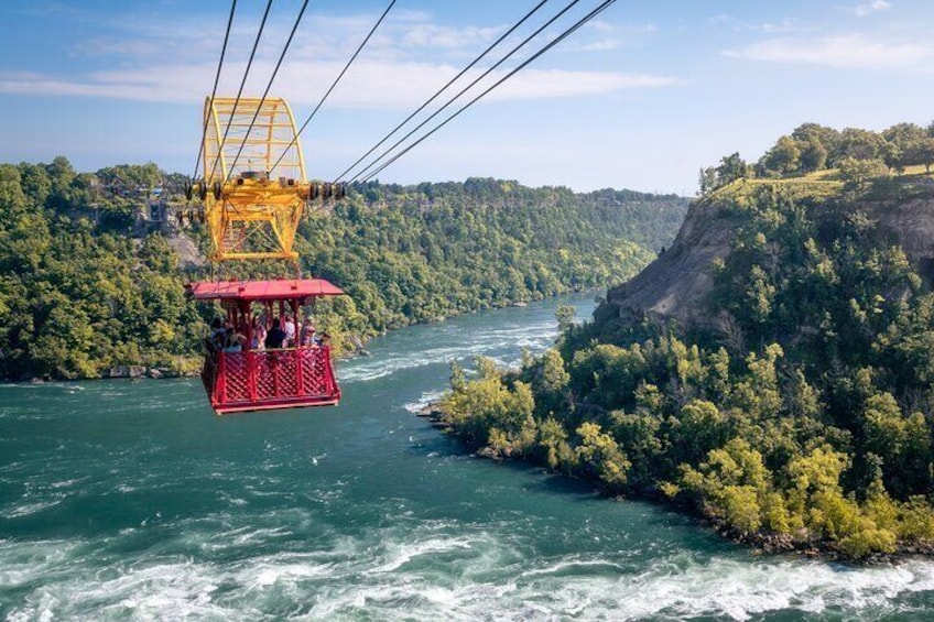 Eine Seilbahn bewegt sich über einem Fluss, umgeben von bewaldeten Hügeln. 5