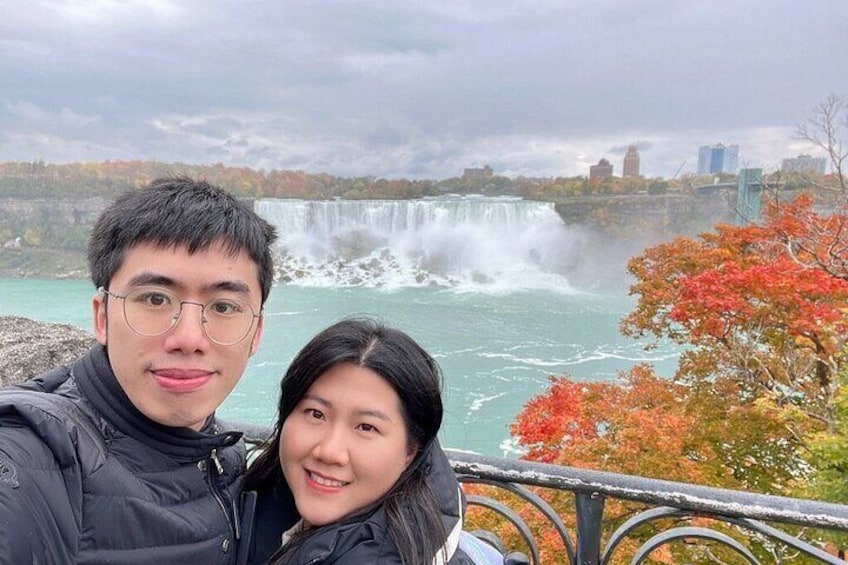 Ein Paar macht ein Selfie vor einem Wasserfall, im Hintergrund Herbstlaub. 4