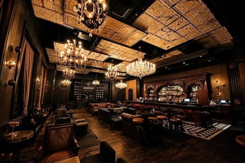 A bar with ornate chandeliers, wooden floors, and a bar area with bottles. 4