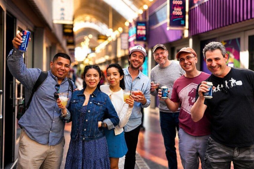 En gruppe mennesker tager en selfie i et shoppingområde med butikker og skilte i baggrunden. 2