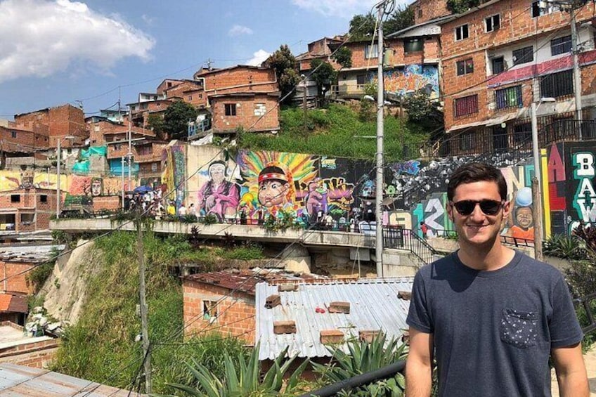 Un hombre de pie frente a un mural colorido en una ladera, con edificios residenciales al fondo. 5