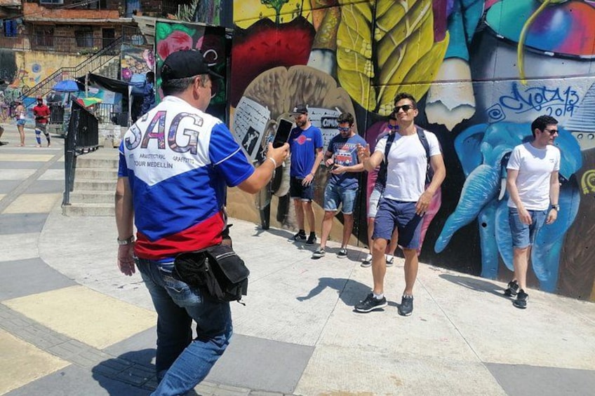 Straßenszene mit einem Mann in blau-rotem Hemd, einer Wand mit bunten Graffiti und Personen, die stehen und gehen. 2