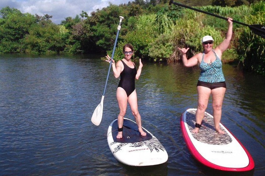 Two people paddleboarding on a river surrounded by greenery. 5